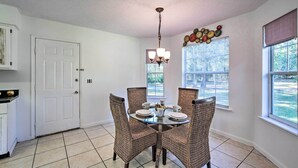 A dining area with a round glass table, wicker chairs, a chandelier, and a window with blinds. - Sunny Abode, 10 Mi to University of Florida! (Gainesville)