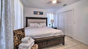 A bedroom with a bed, a nightstand, a lamp, a window, and a door. - Sunny Abode, 10 Mi to University of Florida! (Gainesville)