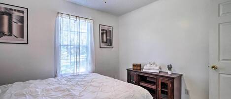 Une chambre à coucher comprenant un lit, un ventilateur de plafond, une fenêtre avec des rideaux, une commode et une porte.
