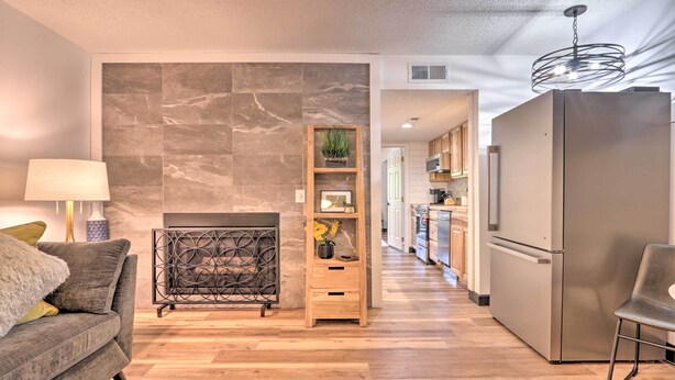 A modern living room with a sofa, a coffee table, a fireplace, a wooden shelf with decorative items, and a kitchen area with a refrigerator and cabinets. - Walk Downtown! Gatlinburg Condo w/ Patio & Pool (Gatlinburg)