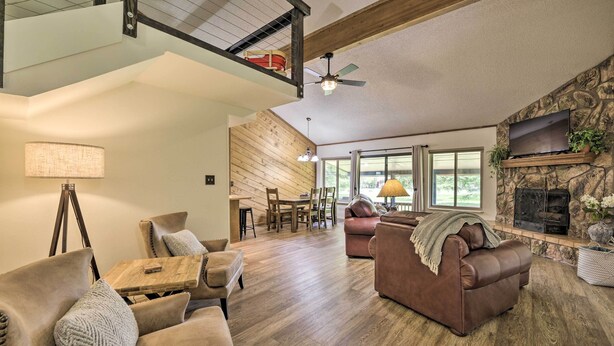A spacious living room with a high ceiling, wooden flooring, a fireplace, and a television mounted on a stone wall.