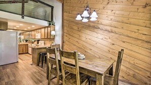 A wooden interior with a dining table and chairs, a kitchen area with wooden cabinets, and a hanging light fixture.
