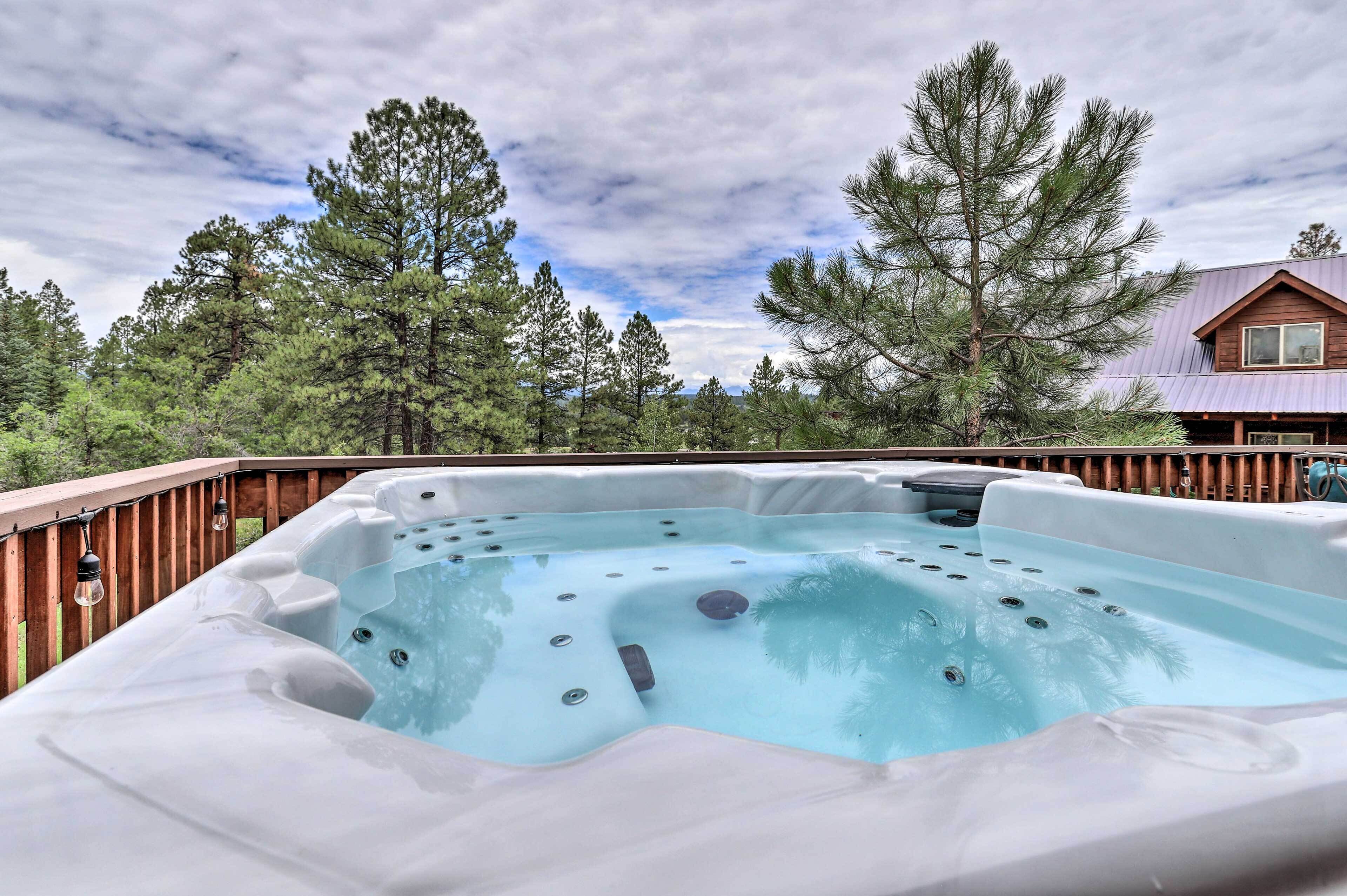 A hot tub surrounded by a wooden deck, with a house and tall trees in the background.