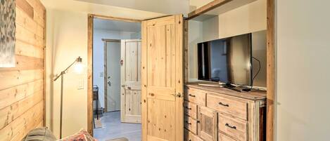 Una habitación acogedora con piso de madera, un sofá, un televisor sobre un mueble de madera y una puerta que da a otra habitación.