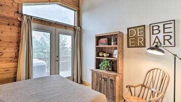 A bedroom with a large bed, wooden walls, a wooden cabinet with books and a plant, a chair, and a wall with 'DEER BEAR' framed artwork.