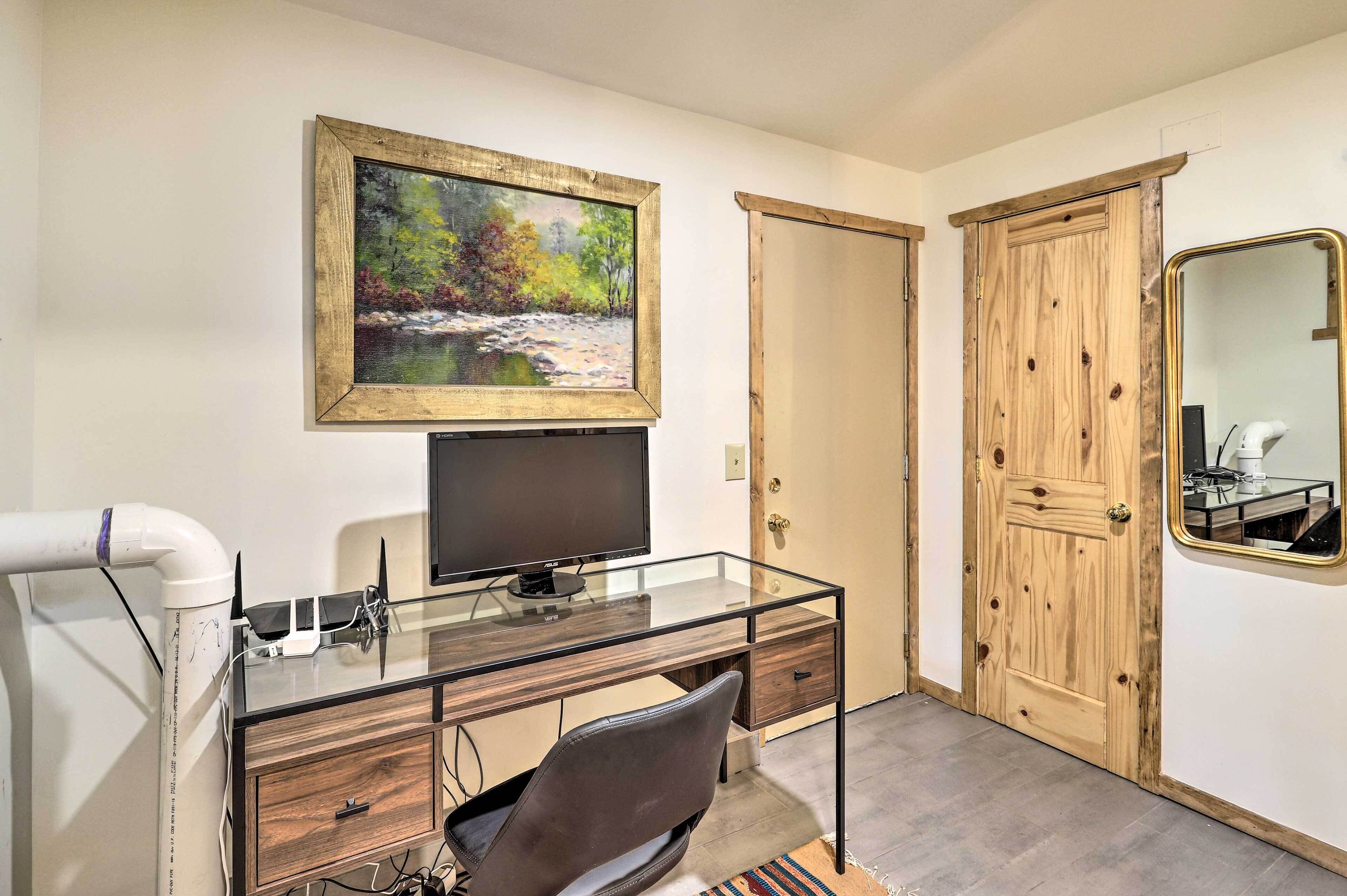 Une pièce avec un bureau en verre, une chaise, un téléviseur, un tableau, une porte en bois et un miroir.