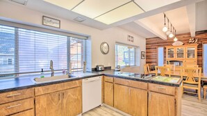 A modern kitchen with wooden cabinets, a dishwasher, and a dining area with wooden chairs and a table. - Pet-friendly Rockaway Beach Home w/ Fire Pit! (Rockaway Beach)