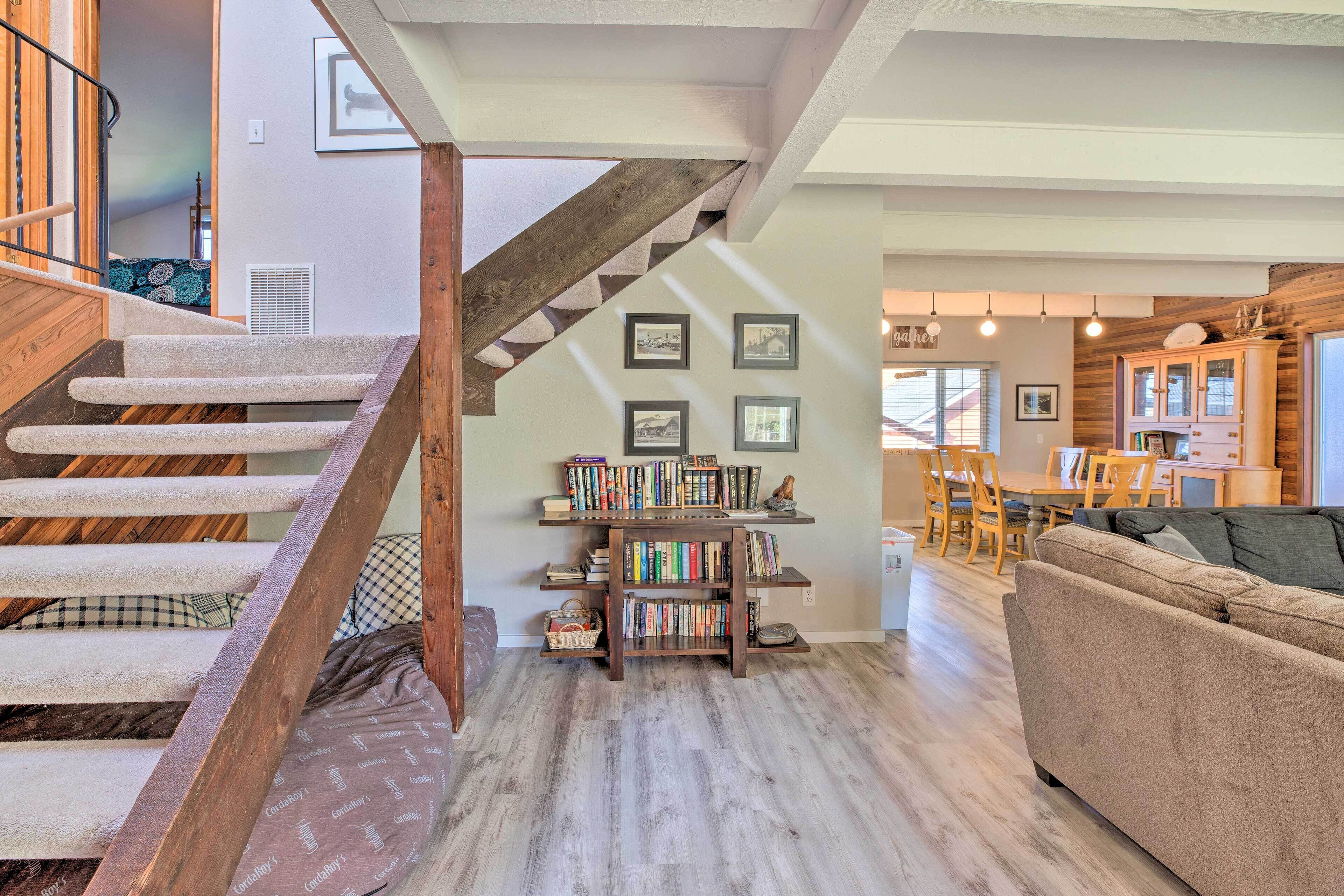 A spacious living area with a wooden staircase, a bookshelf, a sofa, and a dining area.
