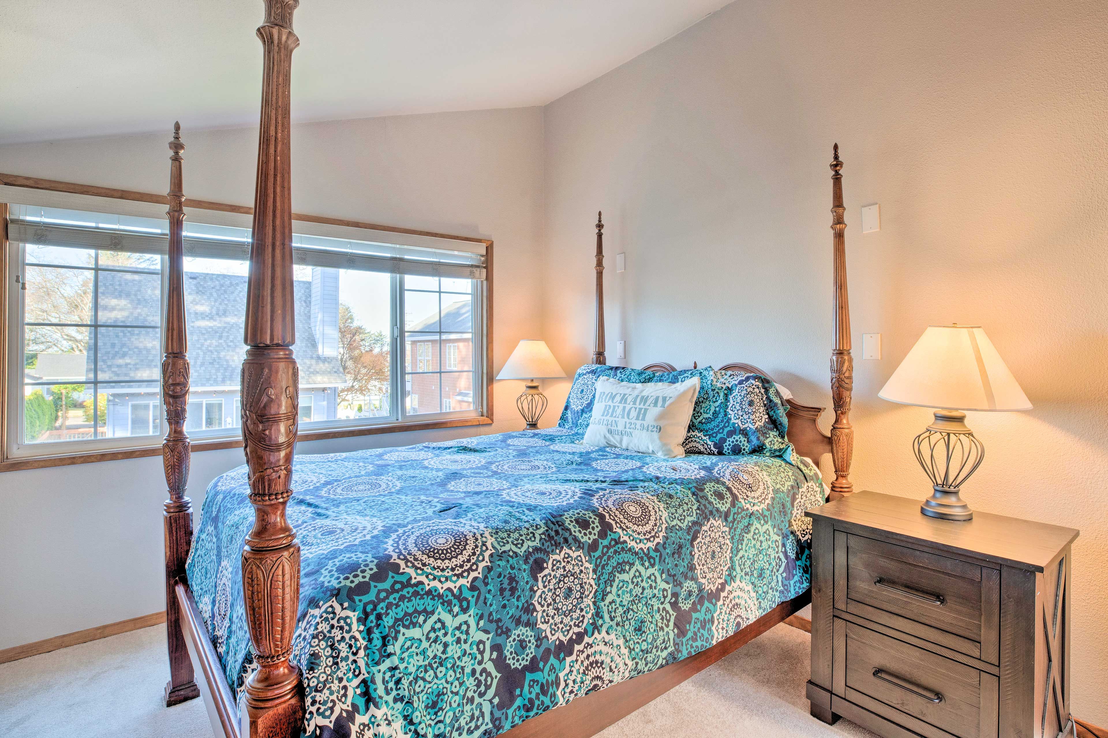 A four-poster bed with a patterned bedspread, bedside tables with lamps, and a window with a view of the outside.