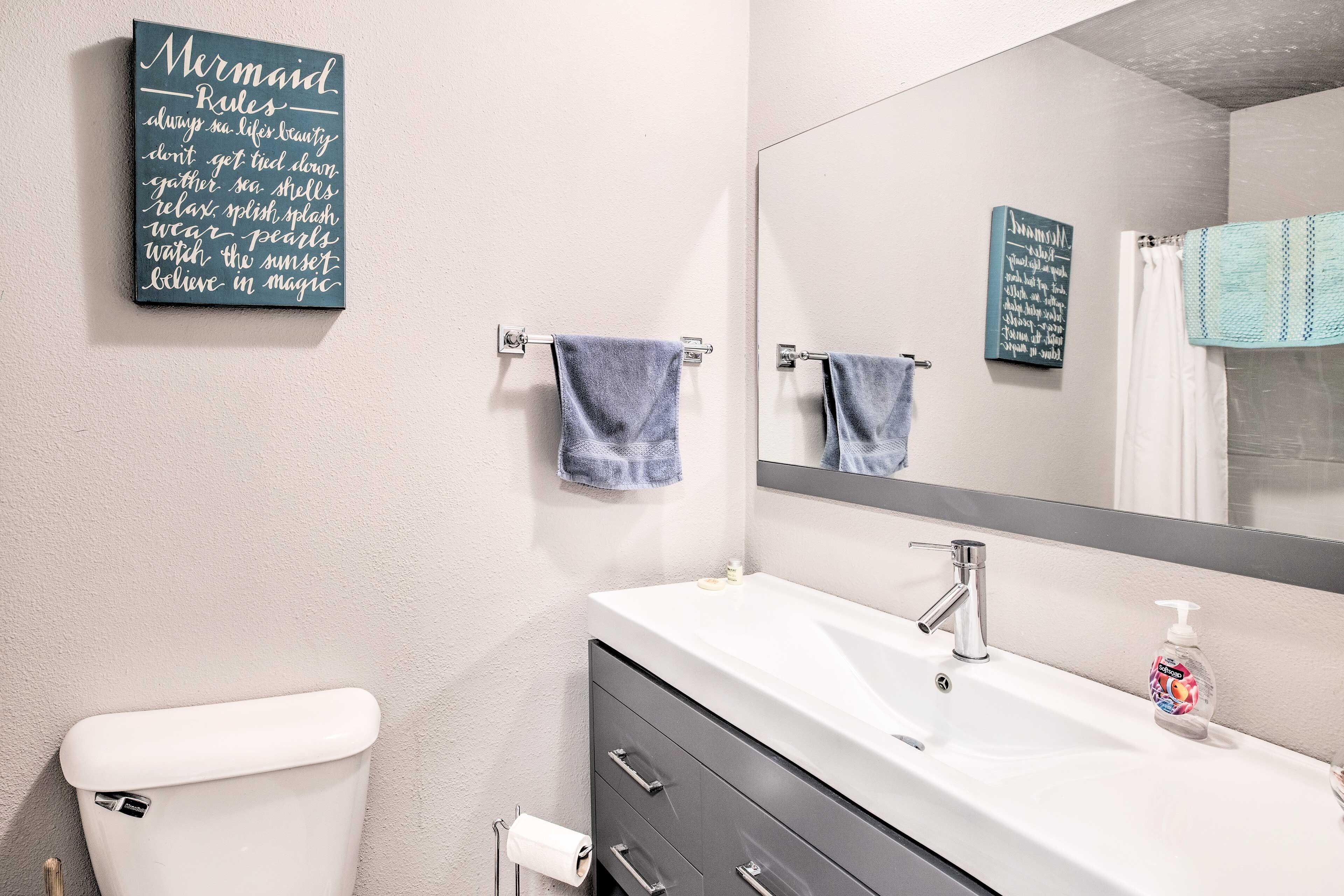 A bathroom with a white sink, a mirror, and two towels hanging on towel bars.