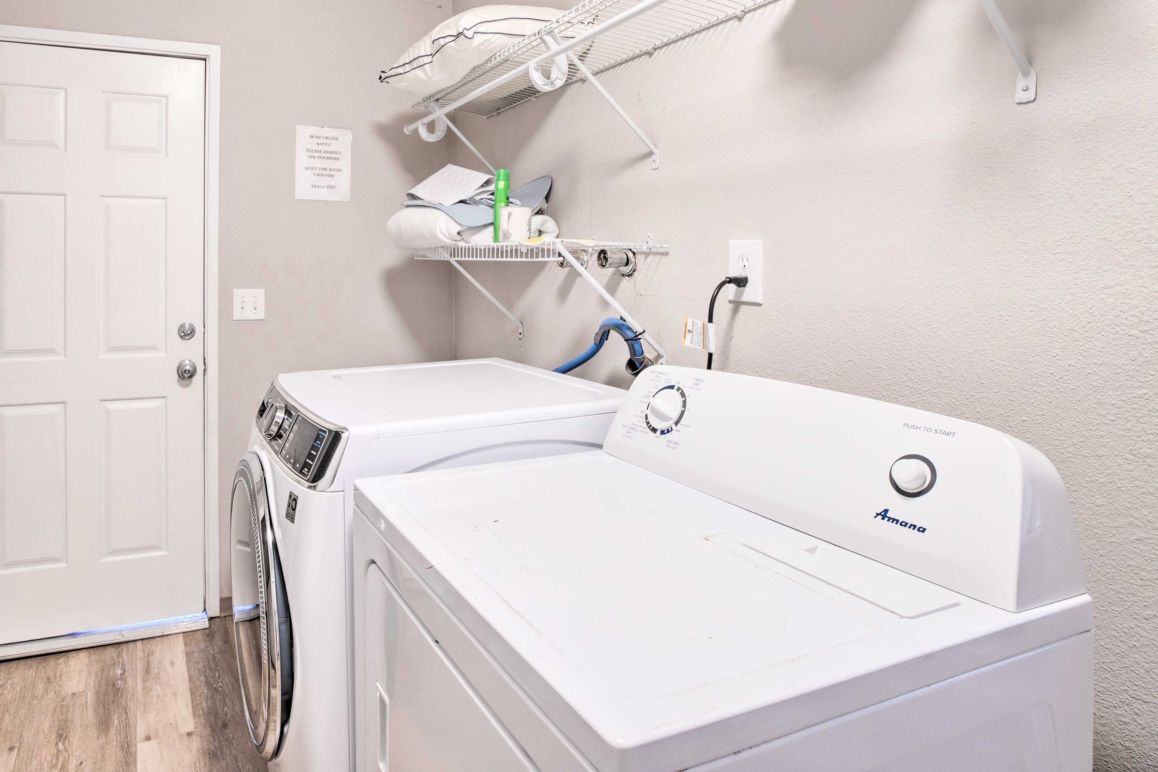 A laundry room with a front-loading washer and dryer, a shelf with laundry supplies, and a door with a sign.