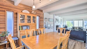 A spacious dining area with a wooden table and chairs, a cabinet with glass doors, and a view of a modern kitchen and living area. - Pet-friendly Rockaway Beach Home w/ Fire Pit! (Rockaway Beach)
