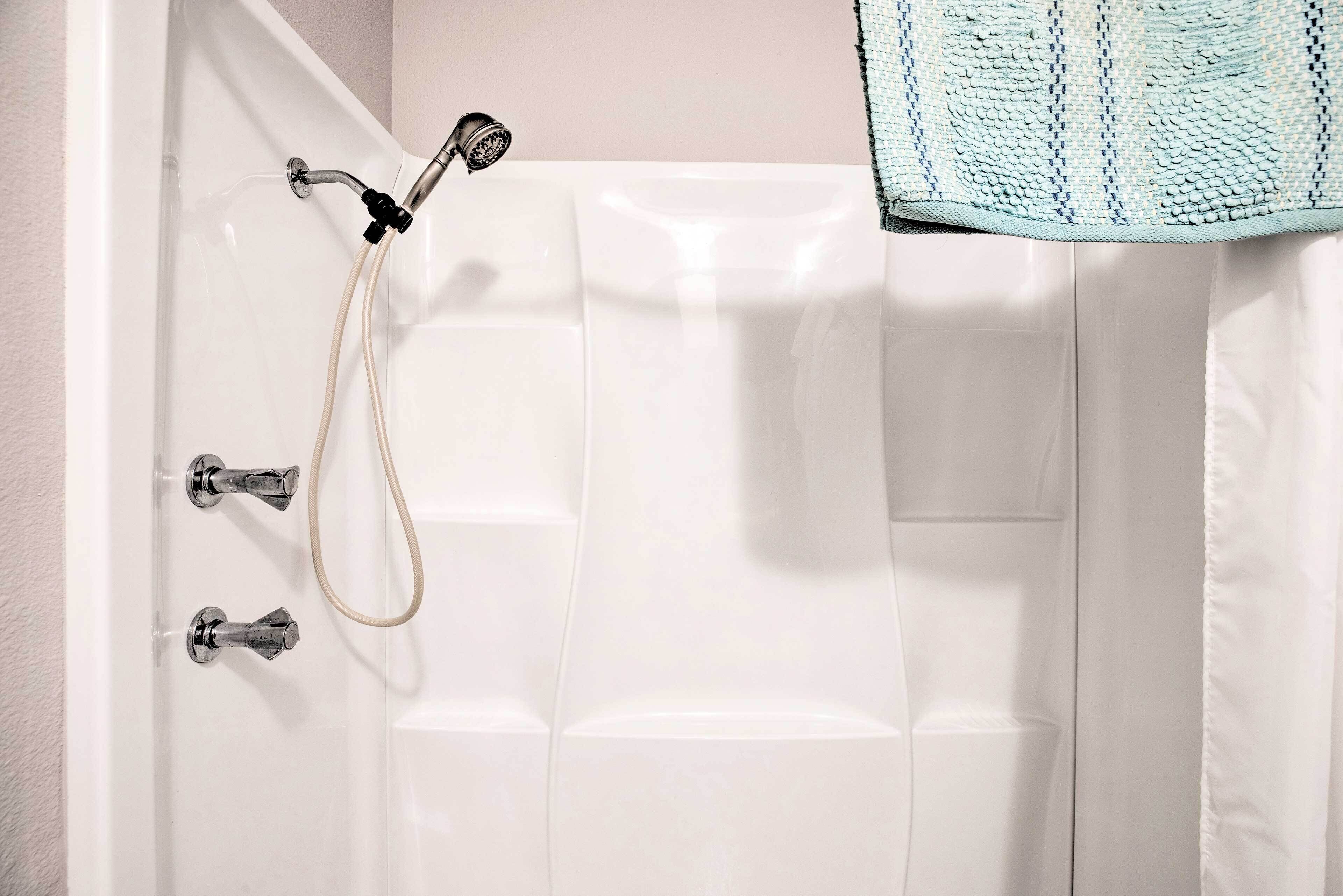 A white bathtub with two faucets and a showerhead, a towel hanging on the wall, and a textured blue towel on the floor.