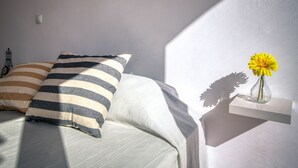 Ein Schlafzimmer mit einem Bett, gestreifte Kissen, einem Nachttisch mit Blumenvase und einem an der Wand befestigten Regal.