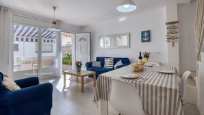 Ein modernes Wohnzimmer mit einem blauen Sofa, einem Esstisch mit gestreiftem Tischläufer und einem großen Fenster mit Blick auf ein Gebäude.