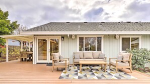 Een overdekt terras met een houten terras, een beige zithoek en een eettafel met stoelen.