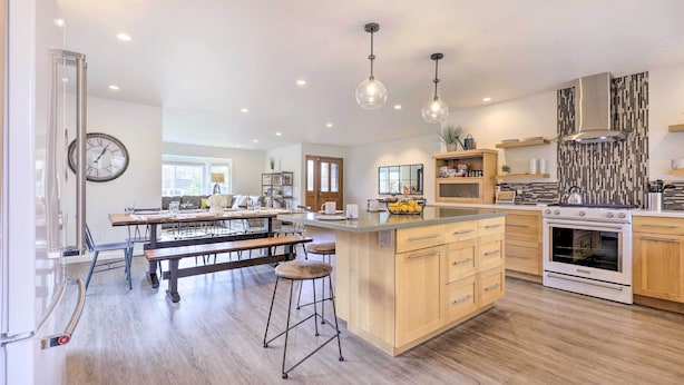 Een moderne keuken met een centraal eiland, houten kastjes, een ingebouwde oven en hangende lampen.