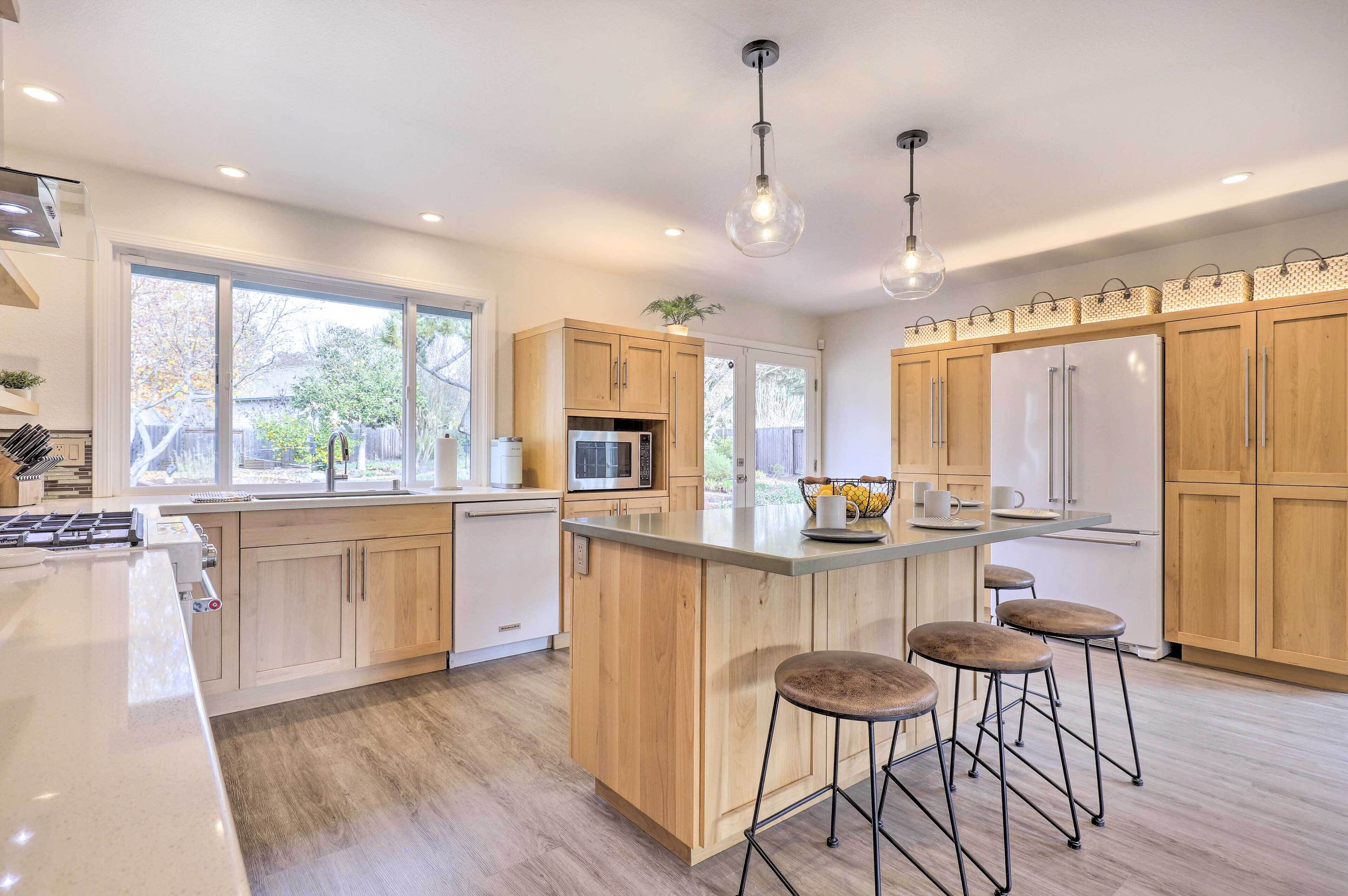 A modern kitchen with wooden cabinets, a central island with stools, a microwave, and a refrigerator.