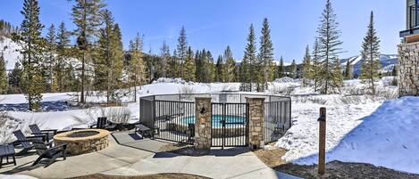 Un espacio al aire libre cubierto de nieve con un hogar de piedra, sillones y una piscina.