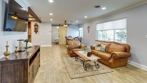 A spacious living room with a wooden coffee table, leather sofas, and a large window providing natural light. - Charming Home w/ Yard ~ 5 Mi to Clearwater Beach! (Clearwater)