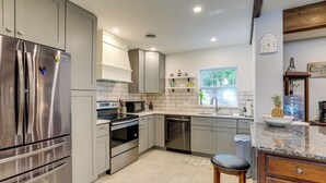 A modern kitchen with stainless steel appliances, grey cabinetry, and a granite countertop. - Charming Home w/ Yard ~ 5 Mi to Clearwater Beach! (Clearwater)