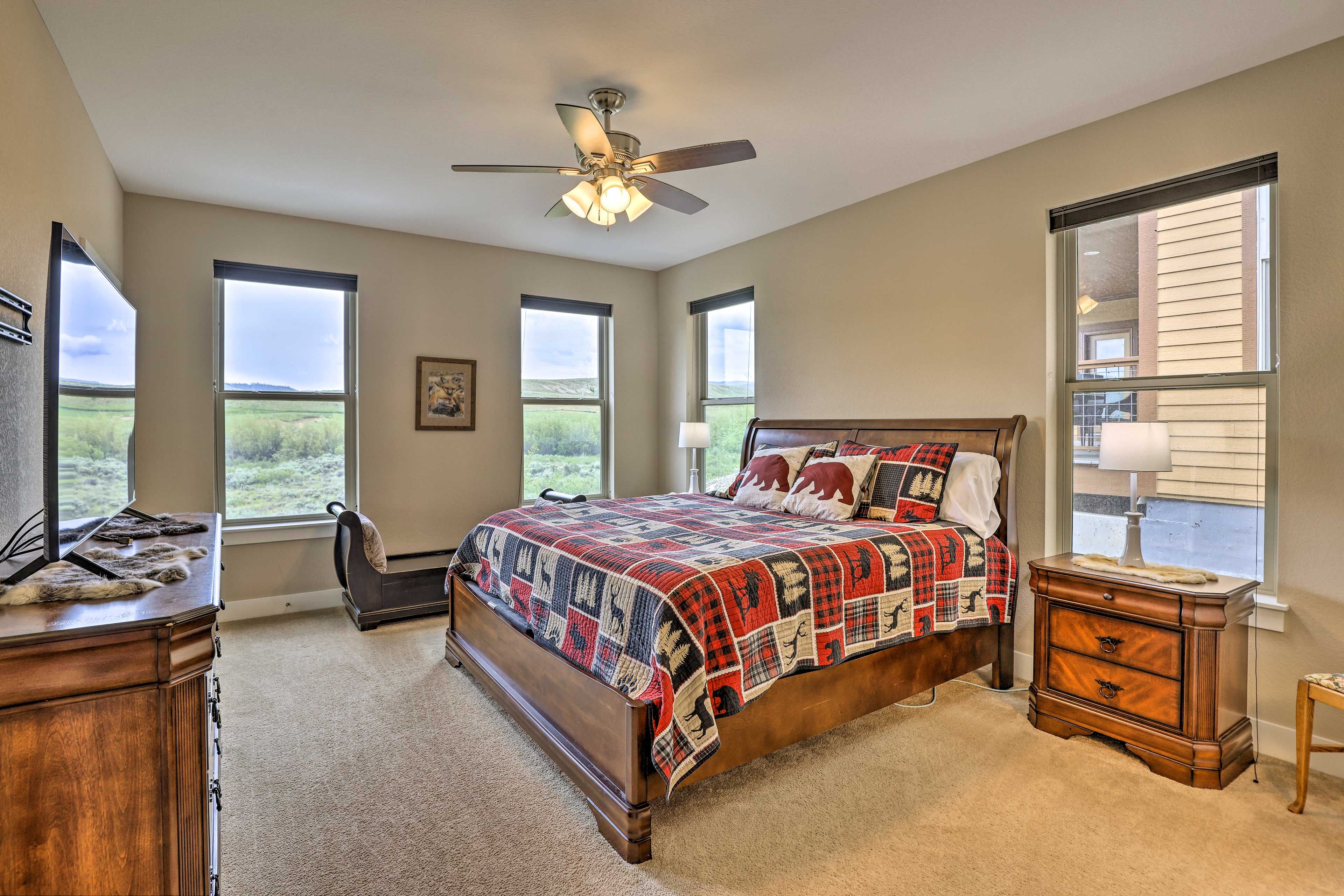 A bedroom with a large bed, a ceiling fan, and a view of the outdoors through the windows.