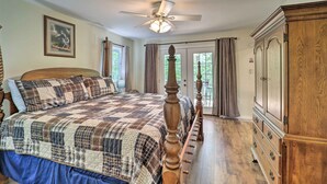 Ein Schlafzimmer mit einem großen Bett, einem Deckenventilator, einer Holzkommode und Blick ins Freie durch eine Glastür.