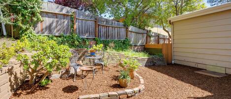 A backyard with a wooden fence, a patio with chairs and a table, and a small garden area with potted plants.