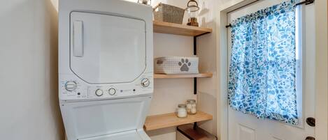 A compact laundry area with a front-loading washing machine, a small shelf with storage items, and a door with a patterned curtain.