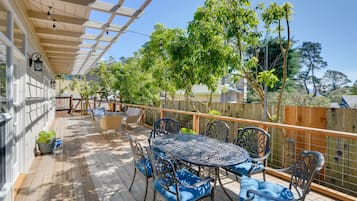 Relax on the covered patio with a round table and comfortable seating, surrounded by lush greenery and a charming pergola.