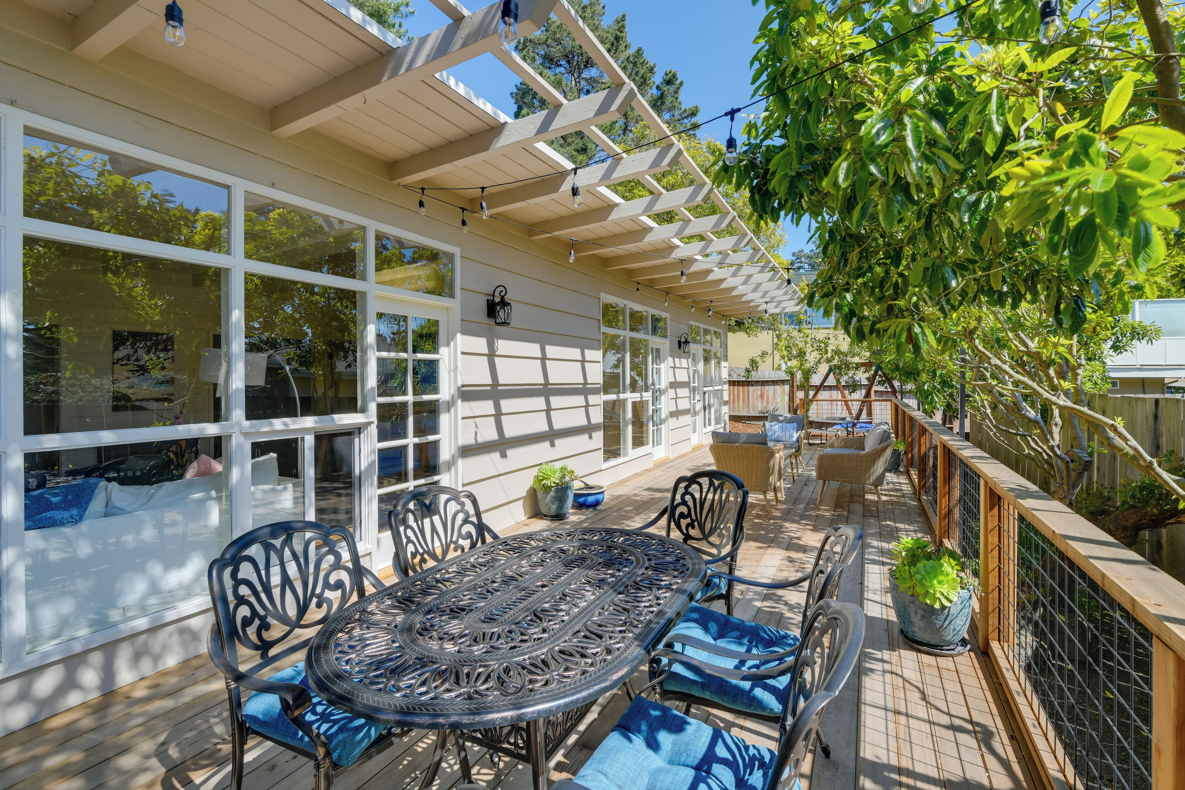 An outdoor patio with a table and chairs, surrounded by potted plants and a pergola.