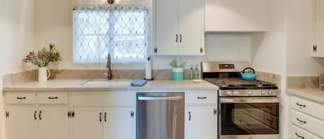 Een moderne keuken met witte kasten, roestvrijstalen apparatuur en een raam met een patroon gordijn.