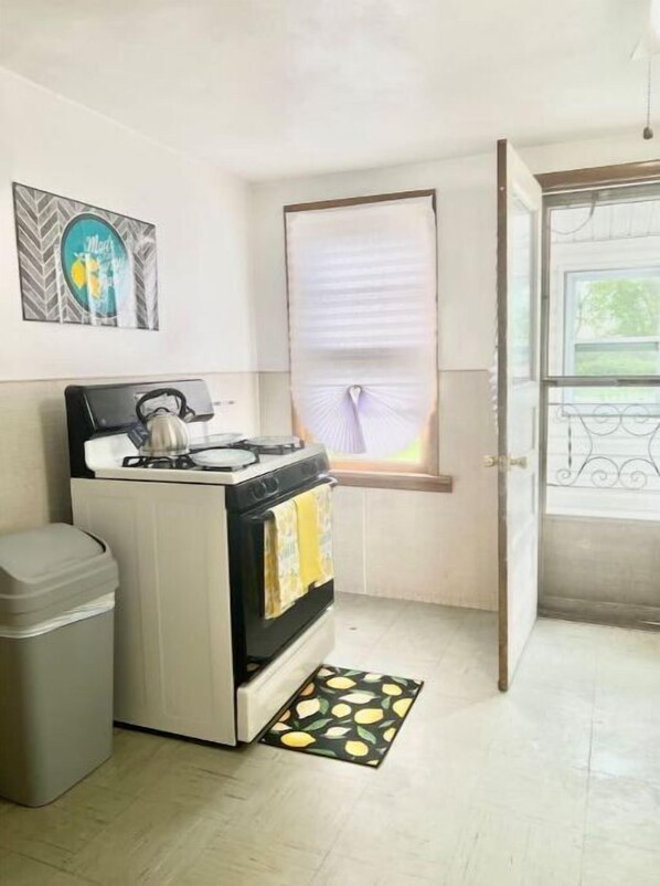 Kitchen area with gas stove, oven, and trash bin, featuring a window and decorative artwork.