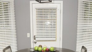 Un comedor con una mesa redonda, dos sillas, una puerta con persianas y una lámpara sobre la mesa.
