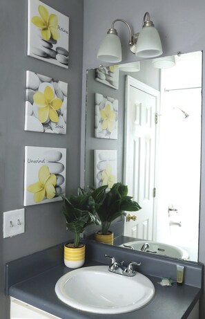 Un baño con lavamanos blanco, dos plantas en macetas y cuadros con flores amarillas.
