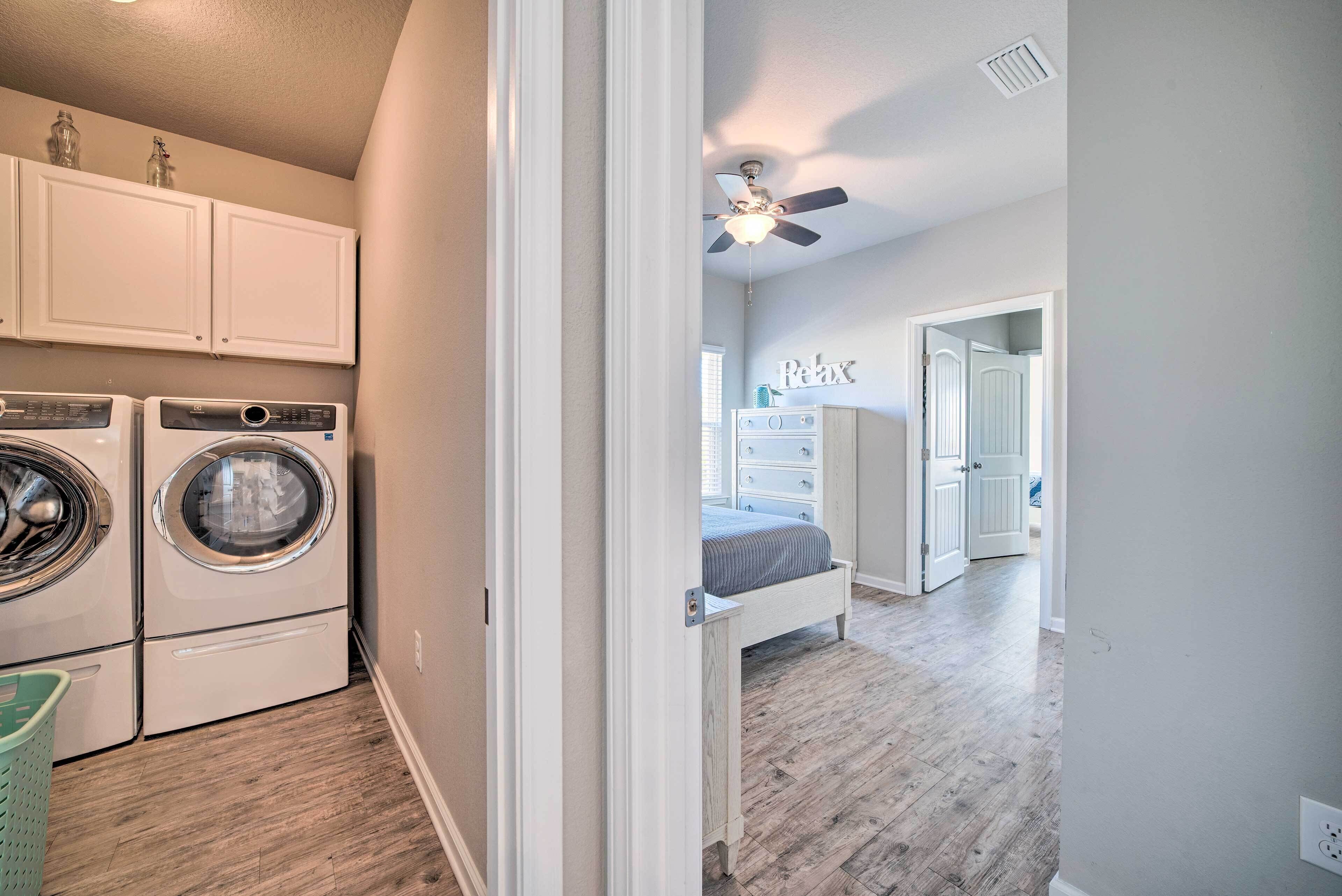 A laundry room with a washing machine and dryer, a ceiling fan, and a hallway leading to a bedroom with a bed and dresser.