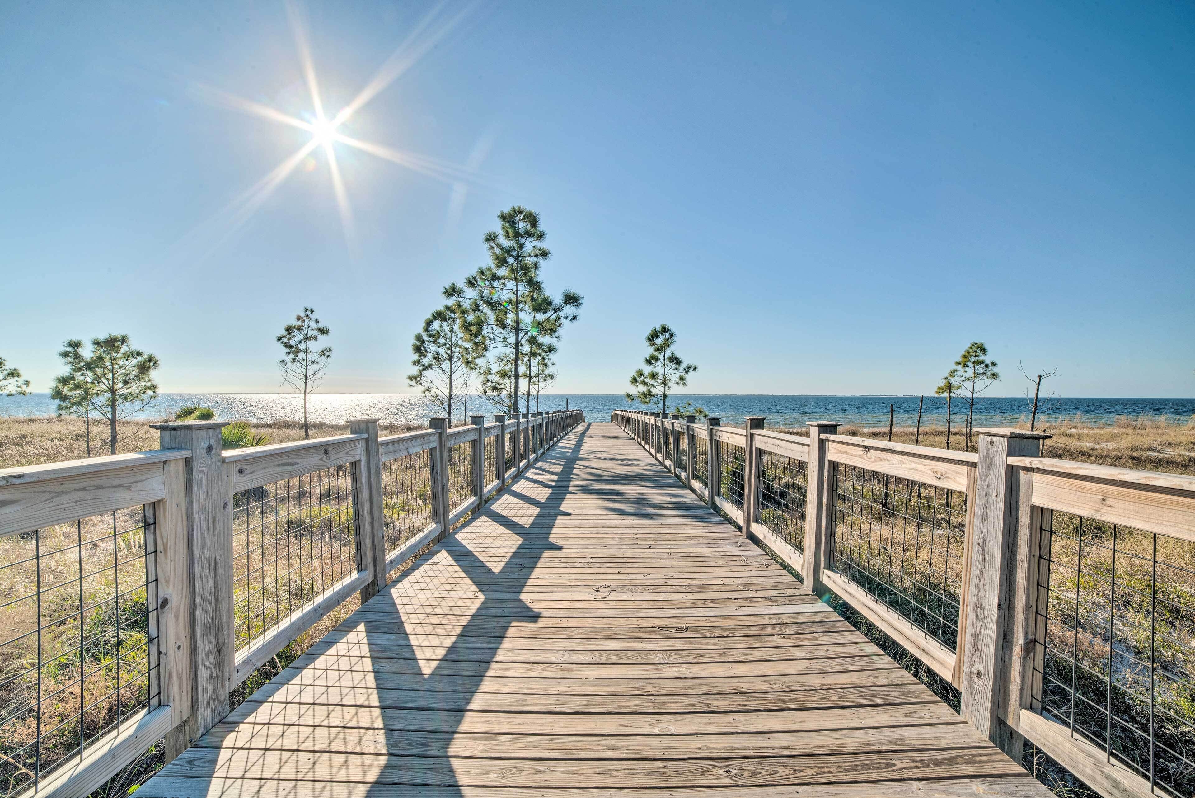 A wooden boardwalk leading to a beach with a clear sky and sun shining.