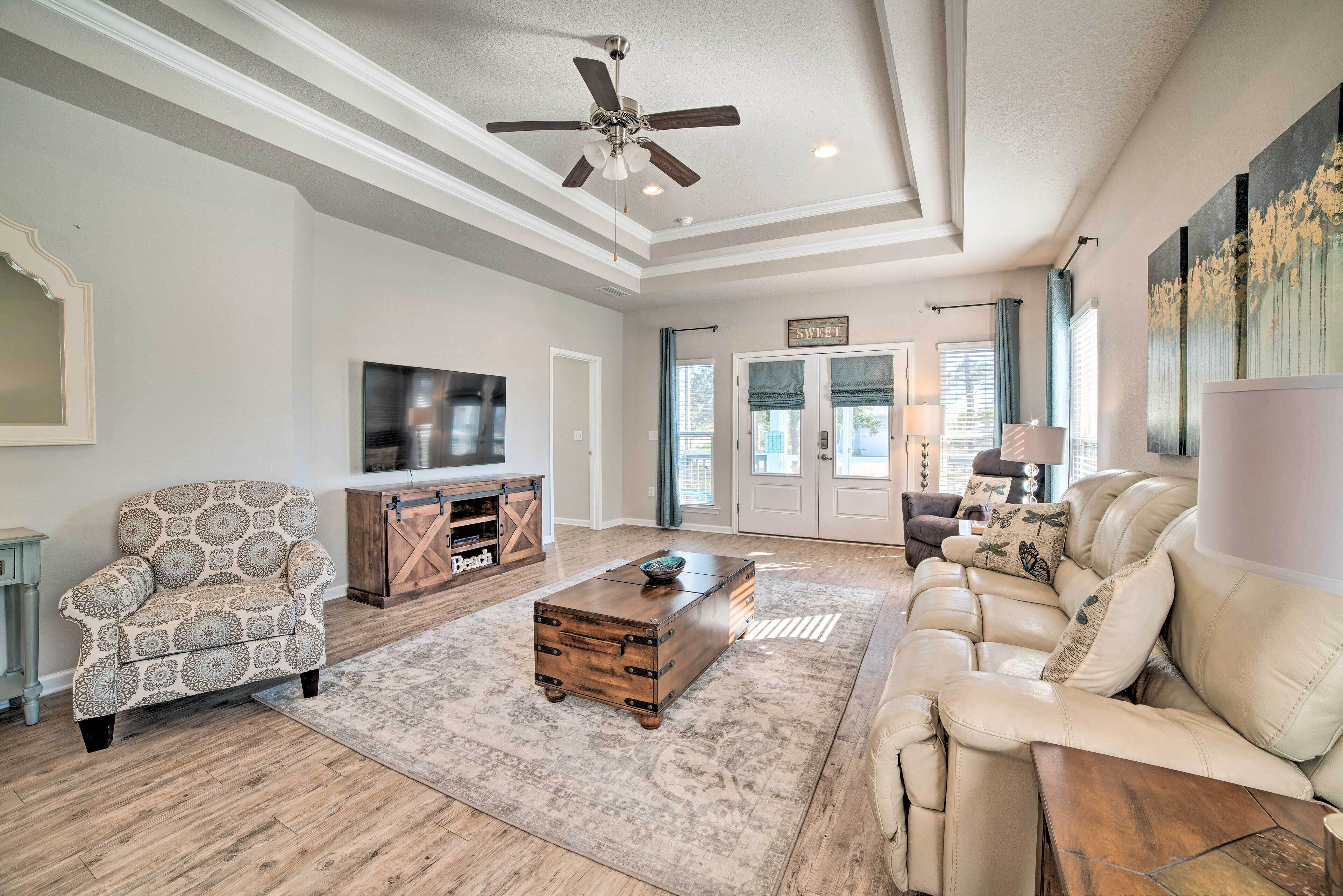 A spacious living room with a large sofa, a patterned armchair, a wooden coffee table, and a television.