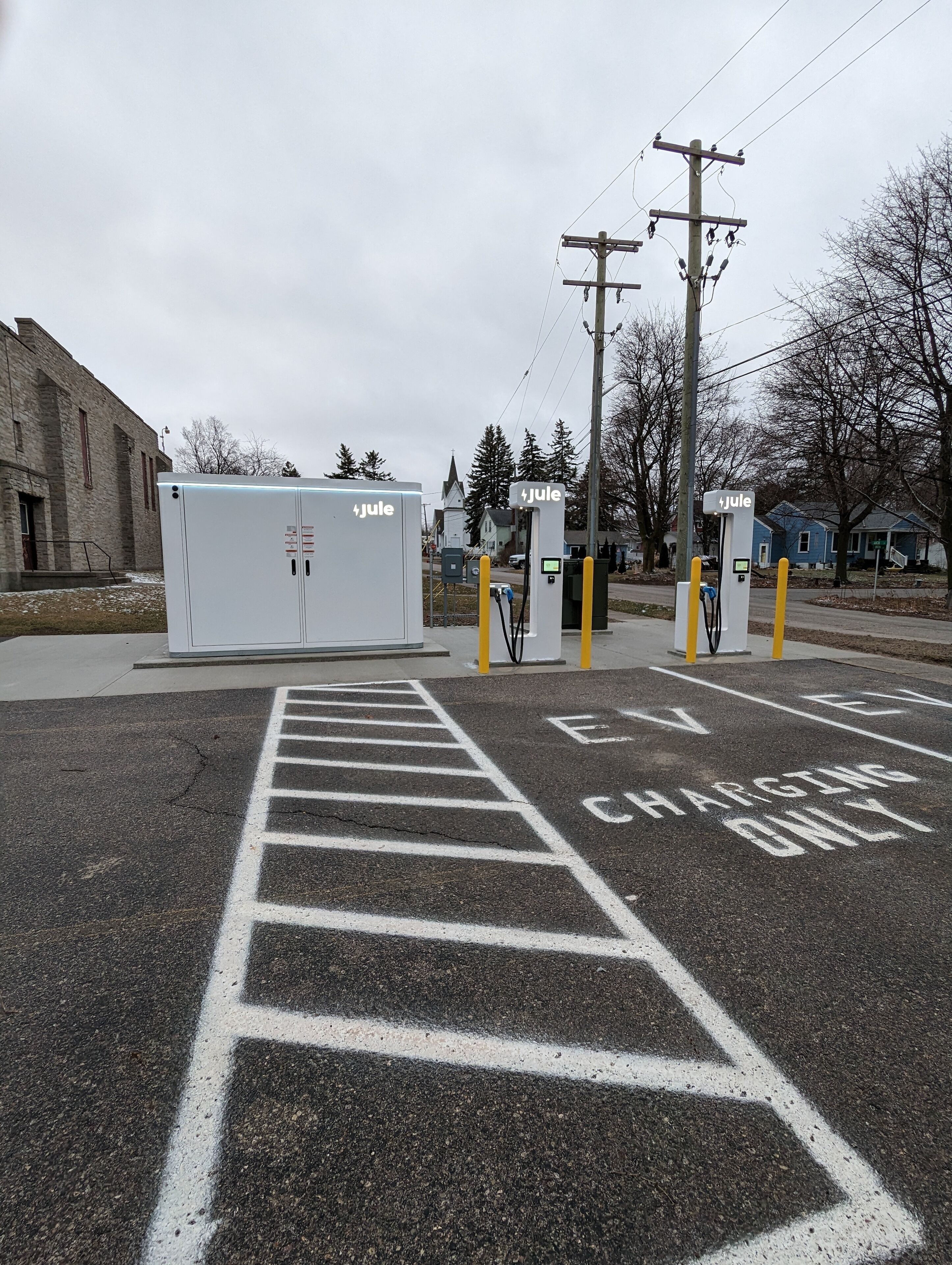 Ein Parkplatz mit Ladestationen für Elektrofahrzeuge, gekennzeichneten Stellplätzen für Elektroautos und einem Gebäude im Hintergrund.