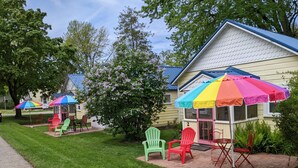 A row of small, single-story buildings with colorful umbrellas and Adirondack chairs in front. - Little Yellow Cottages (Port Austin)
