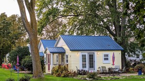 A small yellow house with a blue roof, surrounded by a well-maintained garden and outdoor seating area. - Little Yellow Cottages (Port Austin)
