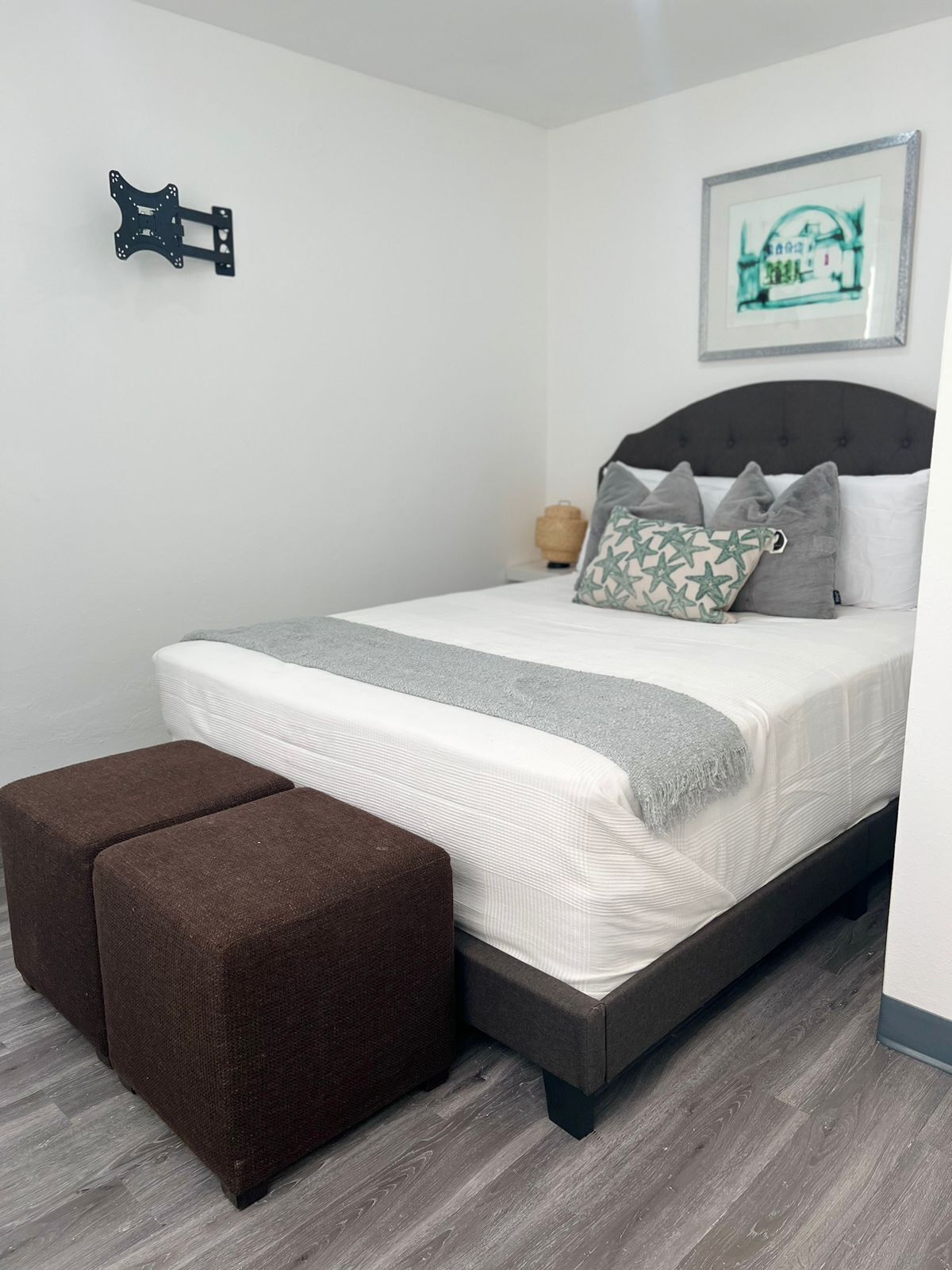 A neatly arranged bedroom with a bed, pillows, a bedside table, and a wall-mounted light fixture.