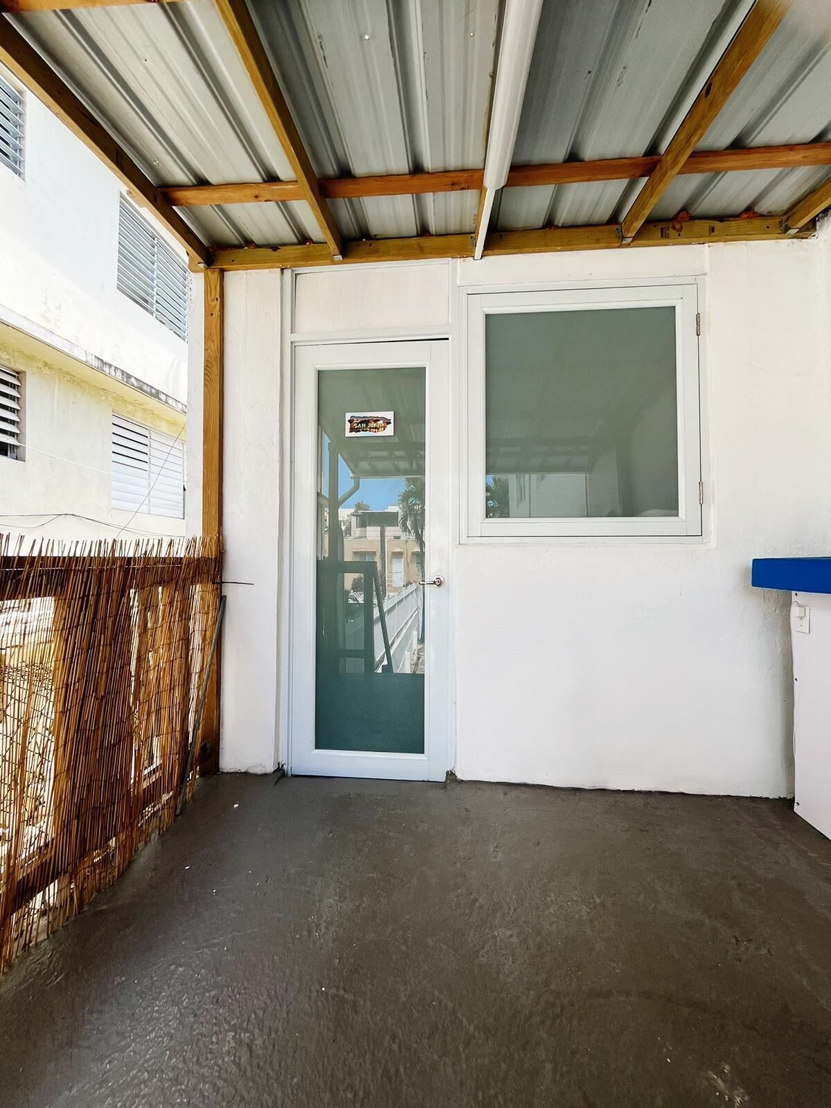 A covered outdoor area with a metal roof, a door with a frosted glass panel, and a blue counter to the right.