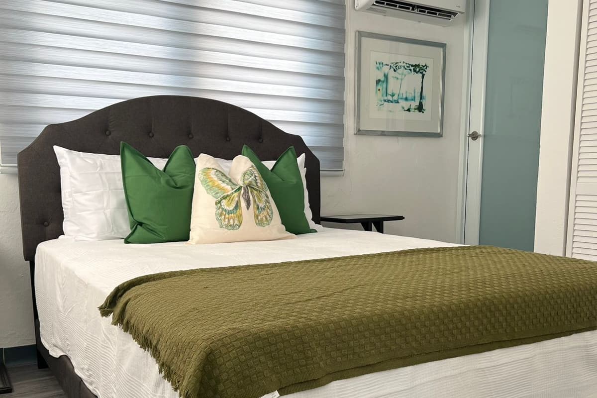 A neatly made bed with a dark headboard, white bedding, and green pillows.