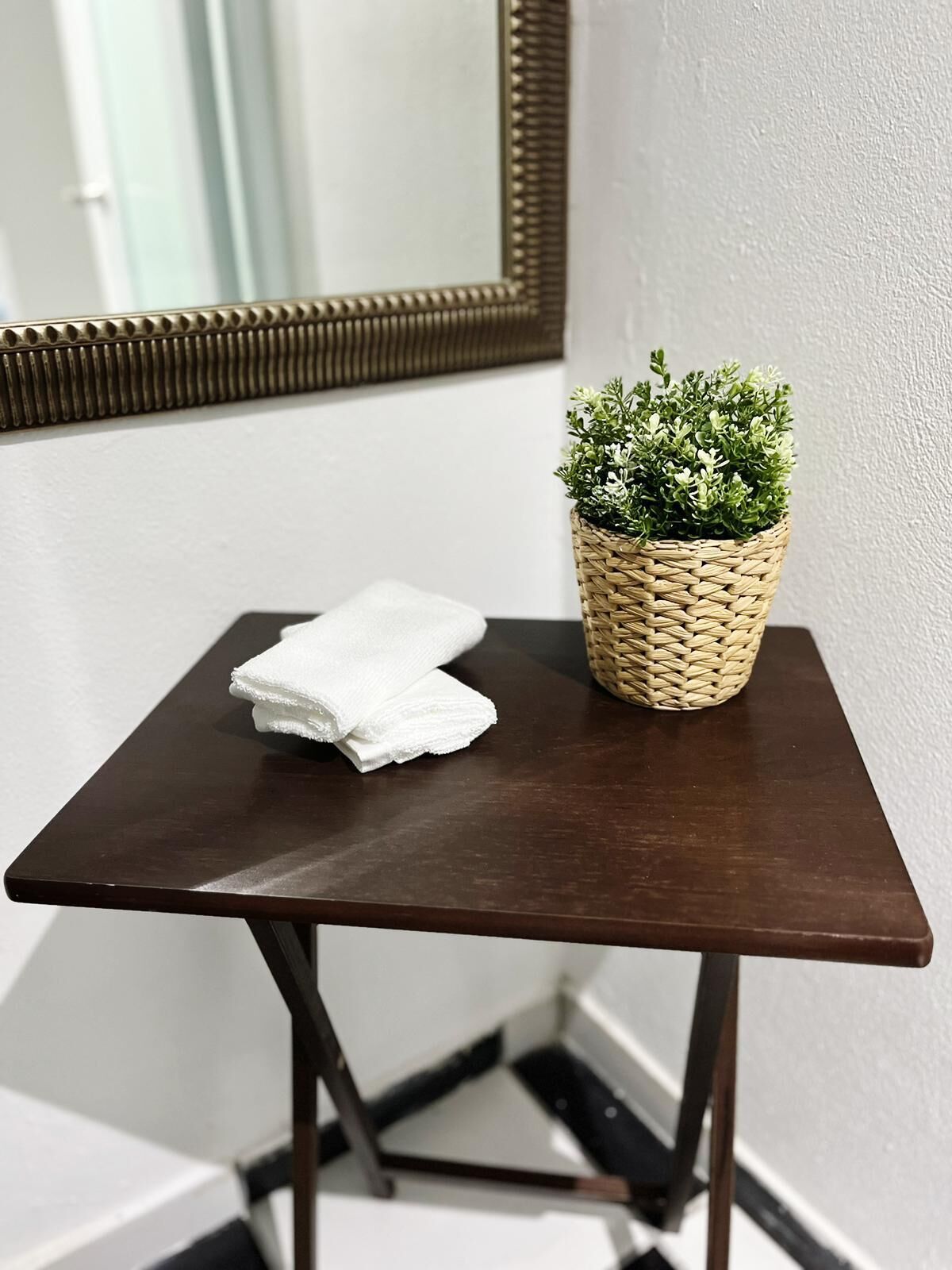 A small wooden table with a woven basket containing green plants and a folded white towel.