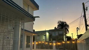 A residential area with a white building, a gated entrance, and a street with a fence. - Janer House (San Juan)