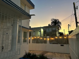 Zona residencial con un edificio blanco, un acceso con puerta de reja y una calle con valla.