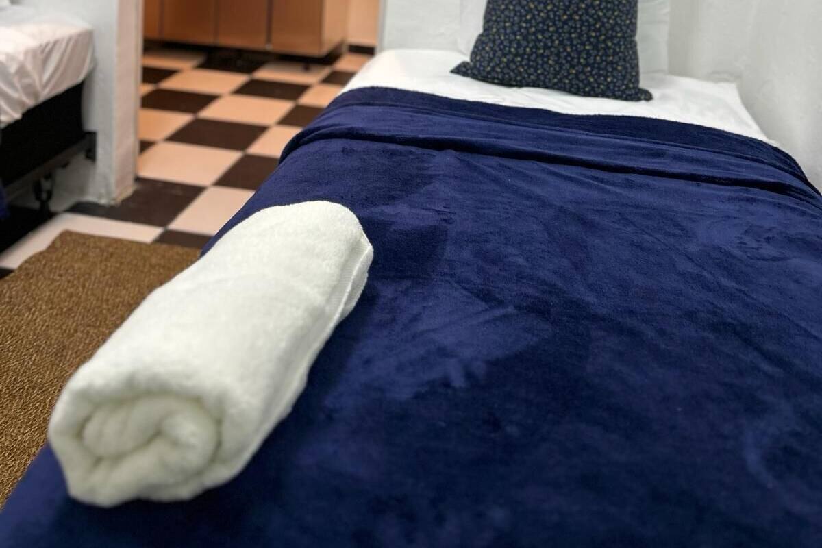 A small, neatly arranged bedroom with a bed, a pillow, and a rolled-up towel.