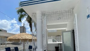 An outdoor patio with a table and chairs, a thatched umbrella, and a white gate leading to an interior space. - Janer House (San Juan)