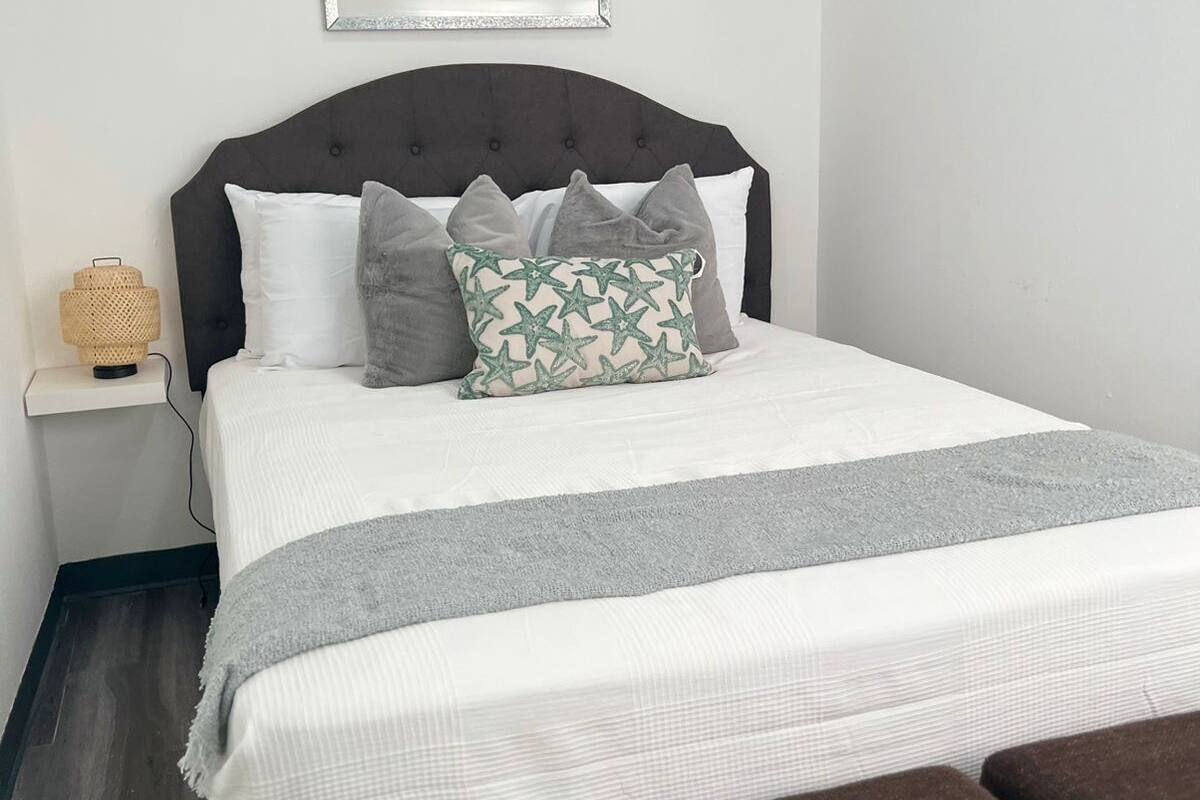 A neatly made bed with a grey and white striped blanket, a dark headboard, and multiple pillows.